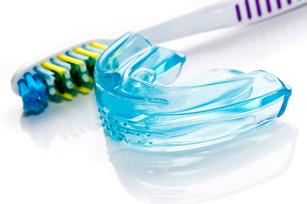 A toothbrush sits on a surface next to a silicone mouthguard.
