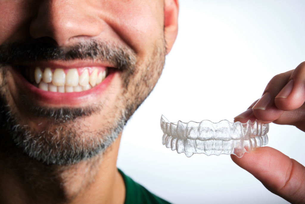 A smiling, bearded adult male holding his Invisalign® aligners in his left hand.
