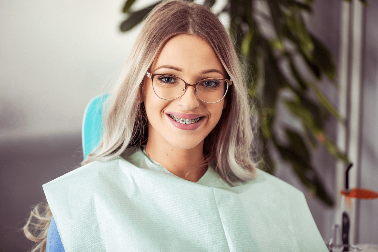Young woman wearing metal braces smiling while sitting in a dental chair.