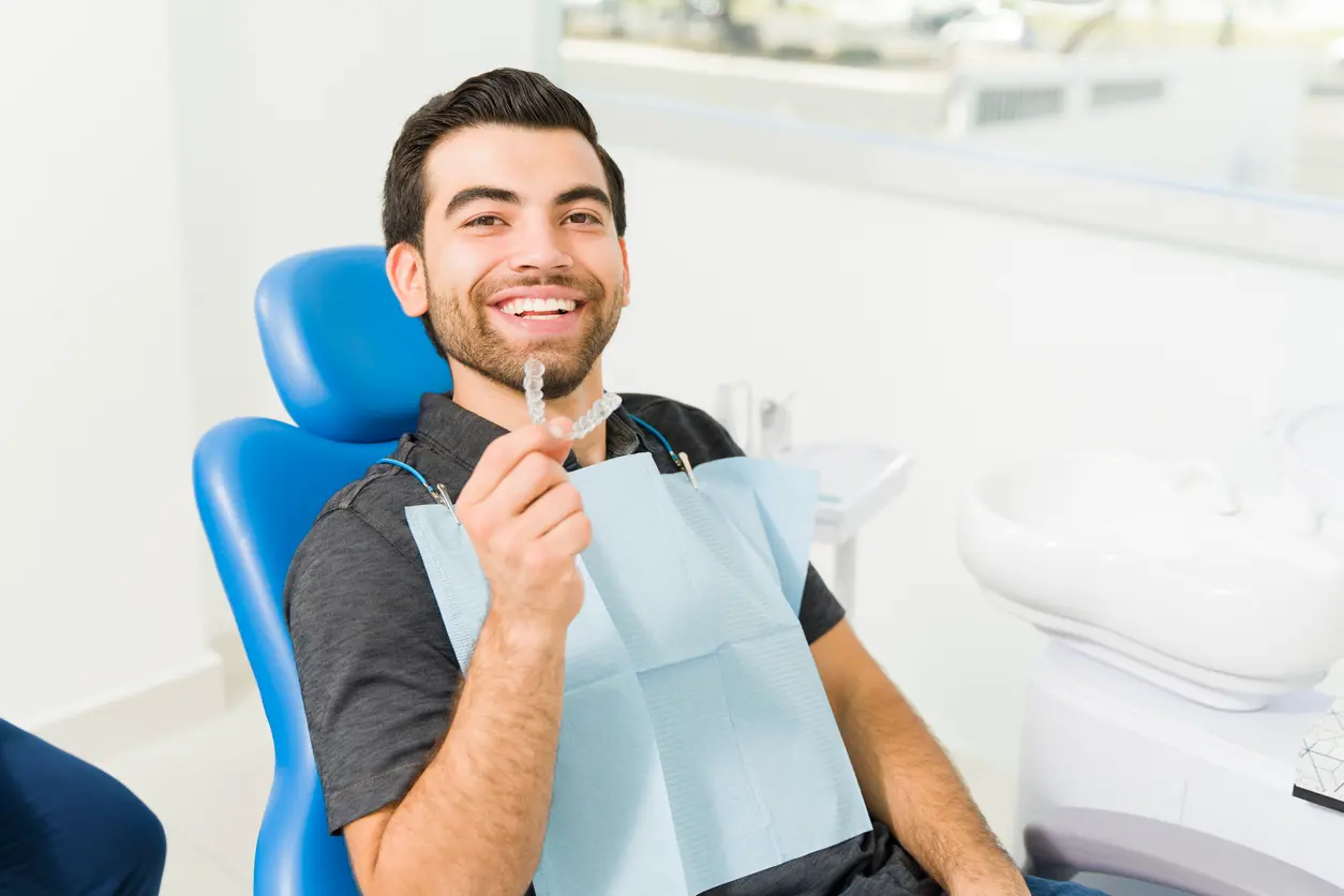 Smiling young man in a dental chair holding an Invisalign® aligner.